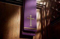 Purple stole with cross lightened by rays of light falling into a confessional.